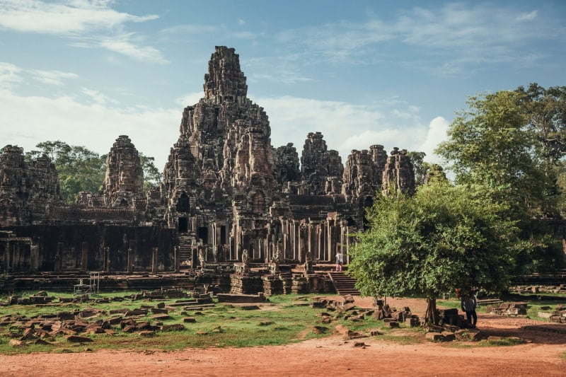 An aerial view of Angkor Wat temple surrounded by growing trees under blue bright sky