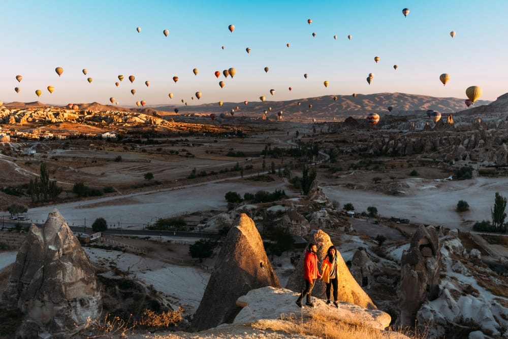 Man and woman greet the dawn among balloons. Couple in love among balloons. Travelers in the mountains of Cappadocia, Turkey. Man and woman traveling. Flying on balloons. Festival of balloons